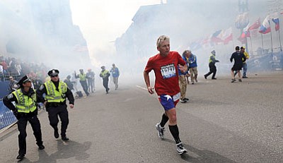 Ken McGagh/MetroWest Daily News, AP<br>A Boston Marathon competitor and Boston police run from the area of an explosion near the finish line in Boston Monday.