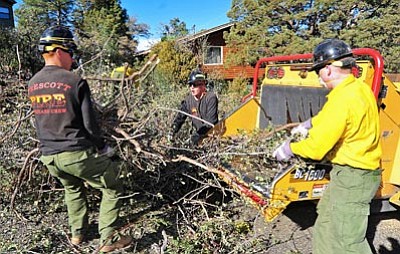 Matt Hinshaw/The Daily Courier<br>Cody Kennedy, Ryan Phillips, and Chris Hewitt, members of the Prescott Fire Department’s Wildland Brush Crew, load limbs, leaves, and debris into a chipper on Vista Ridge Road Wednesday evening in Prescott. The limbs and debris were cut and placed near the roadside by the home owner to be discarded.