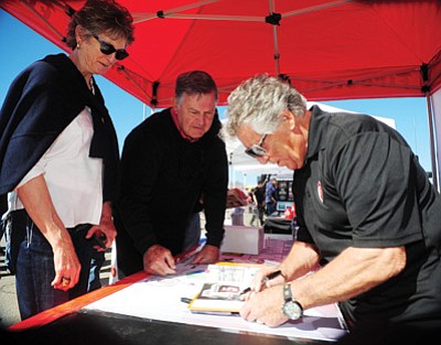 Les Stukenberg/The Daily Courier<br>Mario Andretti signs a book for Peggy and Ryan Falconer at the “Salute to Heroes” kickoff event at Sun Valley Tire in Prescott Valley on Friday. Falconer built engines for Andretti from 1973-76. The event moves to the Prescott Valley Event Center today with free displays and interactives from 1-5 p.m.