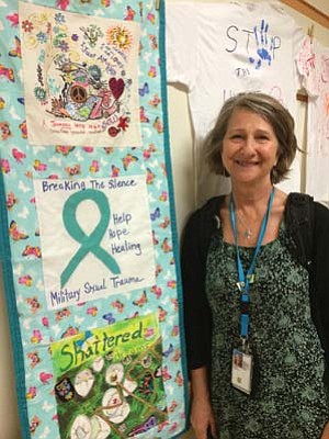 Courtesy<br>Sharon Bowen, licensed clinical social worker and the military sexual trauma coordinator at the Northern Arizona Veteran Affairs Health Care System, stands in front of one of two banner quilts she stitched together. The center square bears the ribbon symbol “Breaking the Silence.’’
