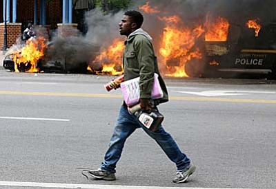 A man carries items from a store as police vehicles burn, Monday, April 27, 2015, after the funeral of Freddie Gray in Baltimore. (AP Photo/Patrick Semansky)