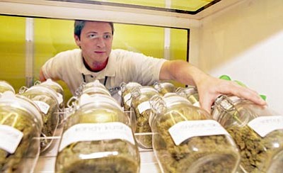Ed Andrieski/The Associated Press<br>Ryan Cook reaches for a jar of medical marijuiana at one of his clinics in Denver.