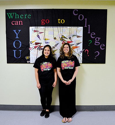 Kingman High School 10th grade GEAR UP student Marlen Alvarez (left) and program coordinator Shelly Moon stand in front of a map labeled with college pennants. (AARON RICCA/Miner)