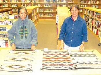 Edith Simonson and Lorraine Herder show several of their completed rugs at the Pinon Accelerated Middle School Library. Their rugs will be on display through May 23 after which they will be sold (Courtesy photo).