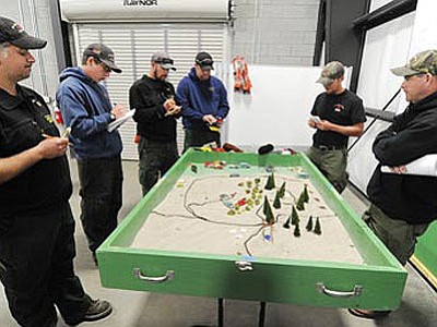 The crew of Prescott National Forest Engine 930 deciphers a wildland fire sandtable scenario presented by PNF Crew 2 Hotshot KC Yowell, at far right, as members of various emergency responder organizations train at the Central Yavapai Regional Training Facility as part of the annual basin drill Friday.<br>
Photo courtesy Les Stukenberg