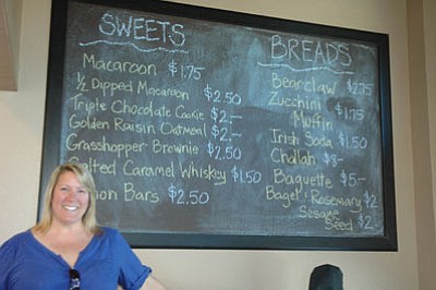 C&C Too owner Sheri Cook stands before the chalkboard menu inside the new deli and bakery that serves up handmade salads, pastries, packaged lunches and soups. (Courtesy)