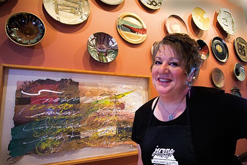 Mary Arkush, owner of the Jerona Café stands with one of her colorful pulp paintings. Arkush will display her artwork at her Jerona Café at a gallery opening on June 27 from 5-7 p.m.