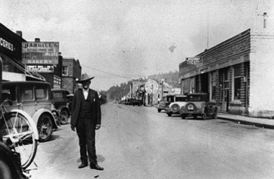 Above:  A man stands on main street in Williams in the 1930s. The image shows the Sultana Theatre, Babbitt’s Grocery, Red Grown Gasoline and the Grand Hotel in the distance. Below: from the same location today. The Sultana is still in the same location, with the Smoke Shoppe on the corner. Babbit’s has been replaced with National Bank of Arizona and Western Wear. Photos/Williams Historical Photo Archive and Wendy Howell/WGCN