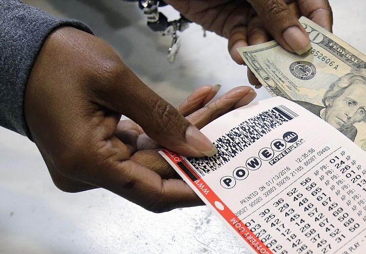 In this Jan. 13, 2016 file photo, a clerk hands over a Powerball ticket for cash at Tower City Lottery Stop in Cleveland. 