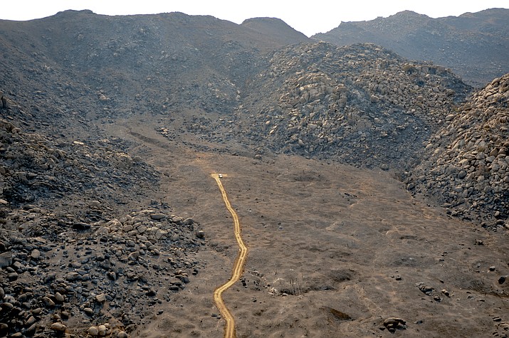 A dozer line can be seen in contrast to the surrounding burned area of the Hotshots’ shelter deployment site near Yarnell. This dozer line was put in to retrieve the bodies of the Granite Mountain Hotshots, it was not created during fire suppression efforts. The deployment site can be seen as a slightly discolored area just beyond the end of the dozer line. 