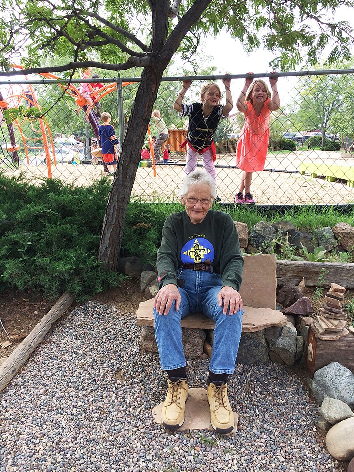 Grandma Susan Calhoun sits on one of the stone benches in the terraced portion of the front garden with second-grader Annabelle Darling and first-grader Valen Graybill peeking in behind her. 