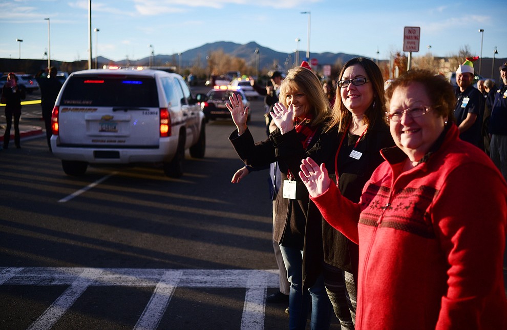 Volunteers Debbie Gatto, Realtor with Realty One Group, Candy Grell,  mortgage monsultant with On Q Financial and Katie Kinon,  mortgage consultant with On Q Financial wave as law enforcement officers from 11 area agencies treated 91 children to a $250. shopping spree as part of the 19th Annual Shop with a Cop at the Prescott Valley Walmart Saturday, December 10.  (Les Stukenberg/The Daily Courier)