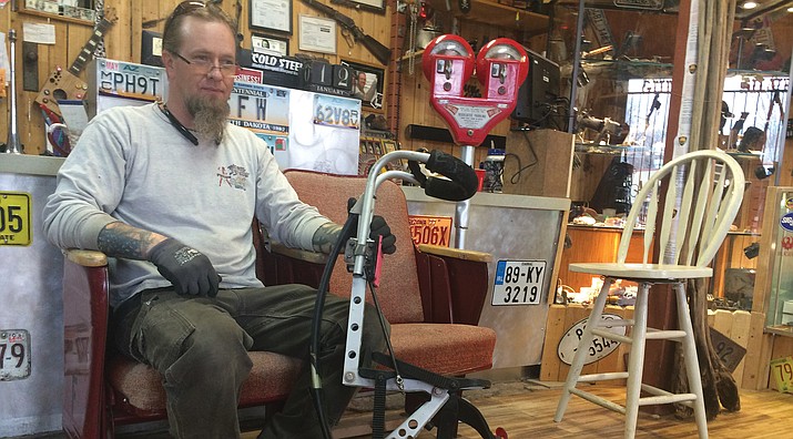 Tom Weisenburger sits on original Elks Theatre chairs, holding bionic legs. Next to the chairs is a parking meter.