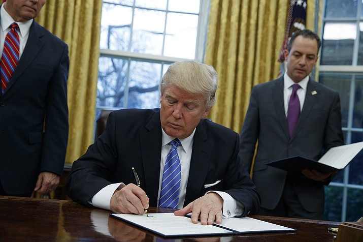 President Donald Trump signs an executive order to withdraw the U.S. from the 12-nation Trans-Pacific Partnership trade pact agreed to under the Obama administration, Monday, Jan. 23, in the Oval Office of the White House in Washington.