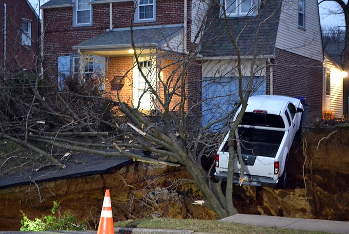 A pickup truck dangles over the edge of a sinkhole the swallowed parts of two residential yards Wednesday morning, Jan. 25, 2017, in the Philadelphia suburb of Glenside, Pa. Officials in Cheltenham Township say the hole, which appears to be about 20 feet deep, opened up about 4 a.m. Wednesday. Authorities say nobody's been hurt and there was no obvious, immediate cause for the sinkhole to develop.