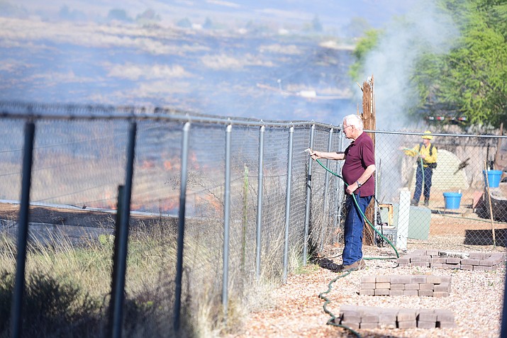 Richard Lavigne uses a garden hose to wet down the area around his home as a wildland fire burns Thursday afternoon on the north side of Manley Drive in Prescott Valley.