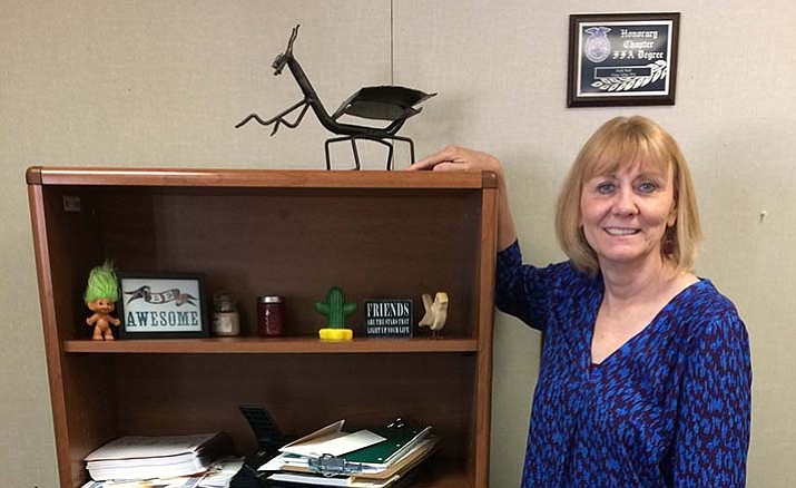 New Chino Valley High School Principal Heidi Wolf stands behind her desk at a bookshelf where a giant welded insect is one of her bookshelf ornaments. It was a gift from some of her students in career education.