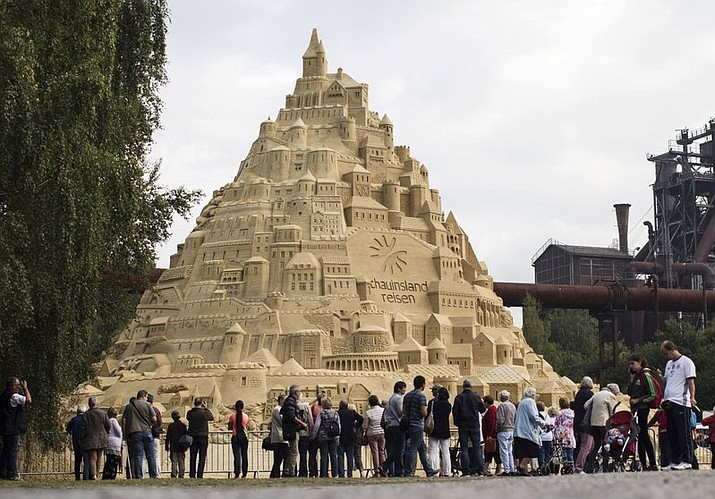 Visitors surround a sandcastle at the Landschaftspark in Duisburg, Germany, Friday, Sept. 1, 2017. Artists attempt to secure a spot in the coveted Guinness Book of World Records by building the tallest sandcastle ever. Later on Friday a jury will arrive to inspect the castle. (Marcel Kusch/dpa via AP)