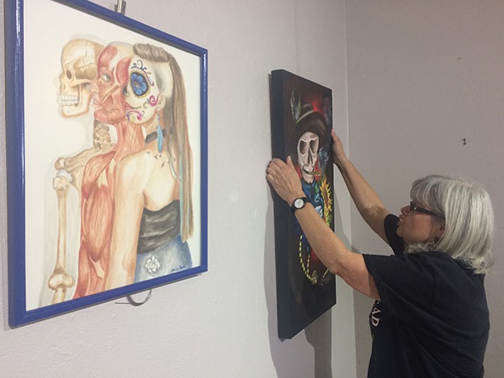 Sukey Jones hangs some artwork from Mexico included in the Day of the Dead exhibit at the Prescott Center for the Arts gallery. (Jason Wheeler/The Daily Courier)