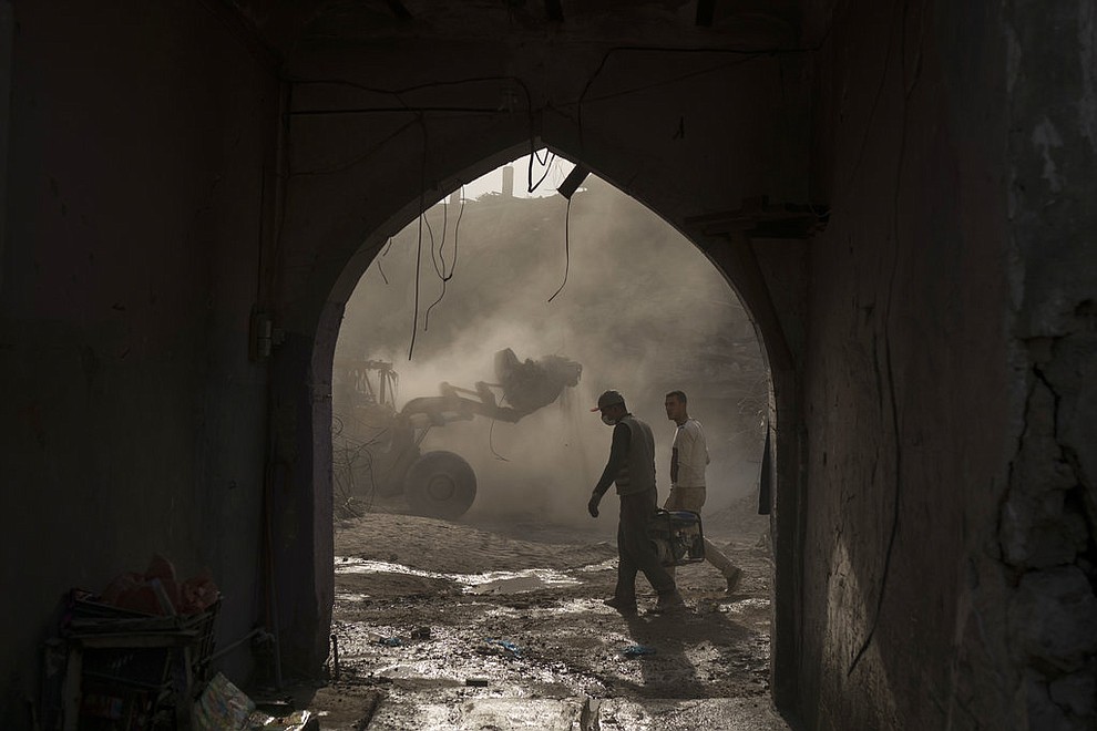 In this Nov. 18, 2017 photo, construction workers carry a generator as a bulldozer remove debris from destroyed shops in the Old City of Mosul, Iraq. Along the neighborhood's gutted roads, a handful of people are beginning to rebuild but the task ahead will take years _ and billions of dollars. (AP Photo/Felipe Dana)