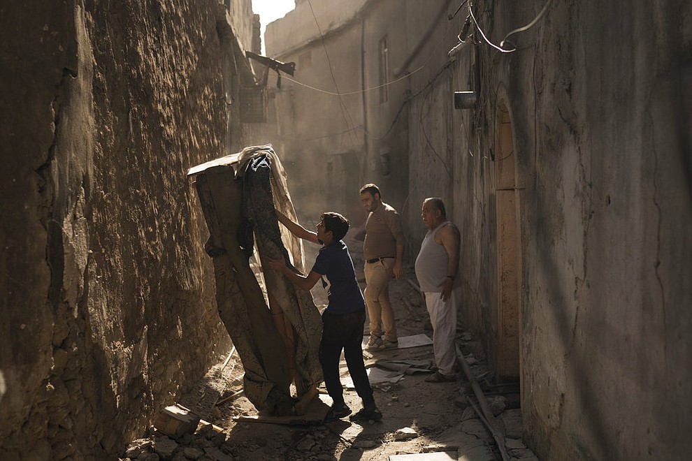 In this Nov. 16, 2017 photo, Mustafa Hansen, left, helps his father Ahmed Mohammed, center, and his grandfather Mohammed Tahar, clear the alley leading to their house in the Old City of Mosul, Iraq. Lacking enough funds from the government or international community, Iraqis have begun to rebuild on their own, dipping into savings and borrowing from friends and family. (AP Photo/Felipe Dana)