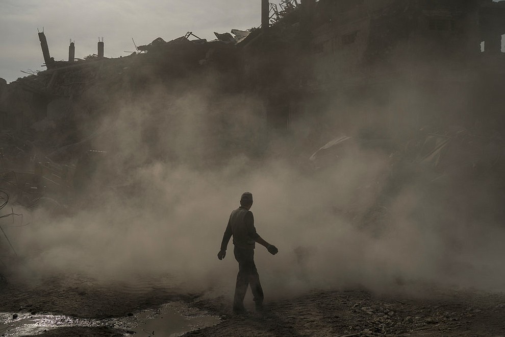 In this Nov. 18, 2017 photo, a construction worker walks amid a cloud of dust as a bulldozer remove debris from destroyed shops in the Old City of Mosul, Iraq. The cost to rebuild after driving out the Islamic State group will be enormous. Baghdad estimates $100 billion is needed nationwide _ while local leaders in Mosul, the group's largest urban stronghold, say that same amount is what's needed in their city alone. (AP Photo/Felipe Dana)