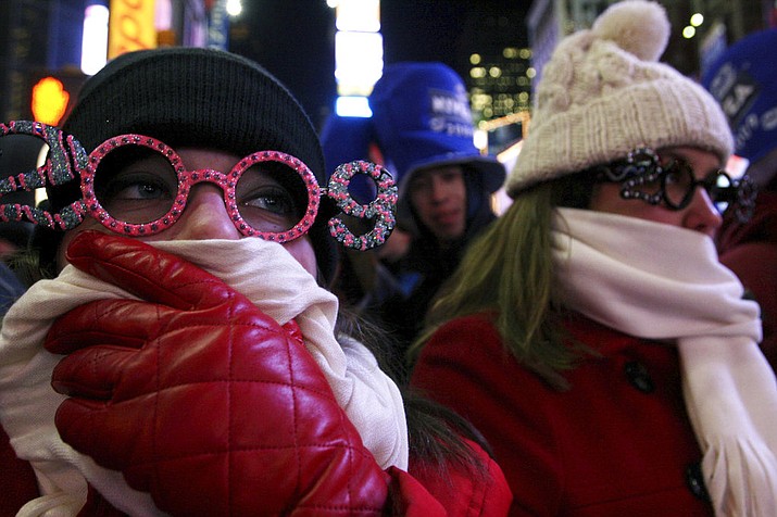 In this Dec. 31, 2008 file photo, Allison Smith of Jacksonville, Fla, left, tries to keep warm as she and others take part in the New Year's Eve festivities in New York's Times Square. Brutal weather has iced plans for scores of events in the Northeast U.S. from New Year’s Eve through New Year’s Day, but not in New York City, where people will start gathering in Times Square up to nine hours before the famous ball drop. (AP Photo/Tina Fineberg, File)