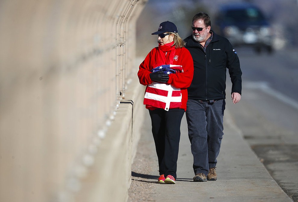 An unidentified couple carry an American flag to hang on the overpass of Colorado Boulevard over Highway C470 before a procession passes with the body of a sheriff's deputy shot and killed while responding to a call Sunday, Dec. 31, 2017, in Highlands Ranch, Colo. (AP Photo/David Zalubowski)