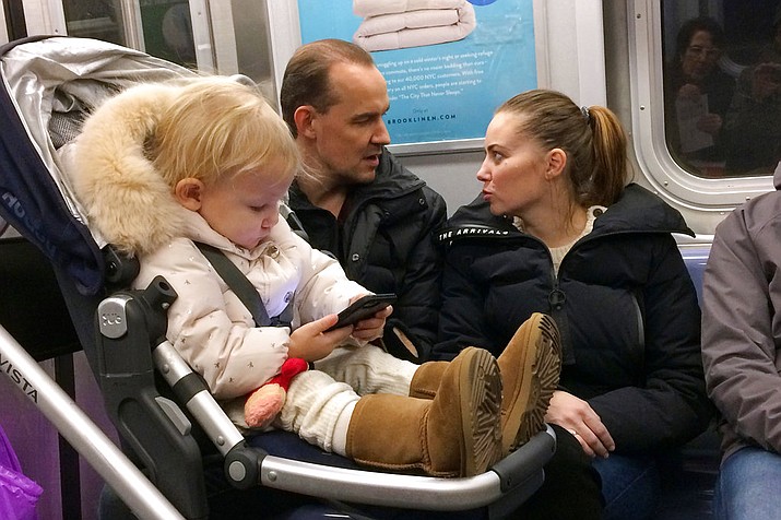 In this Dec. 17, 2017, photo, a baby girl plays with a mobile phone while riding in a New York subway. Two major Apple investors have urged the iPhone maker to take action to curb growing smartphone use among children, highlighting growing concern about the effects of gadgets and social media on youngsters. (AP Photo/Mark Lennihan)
