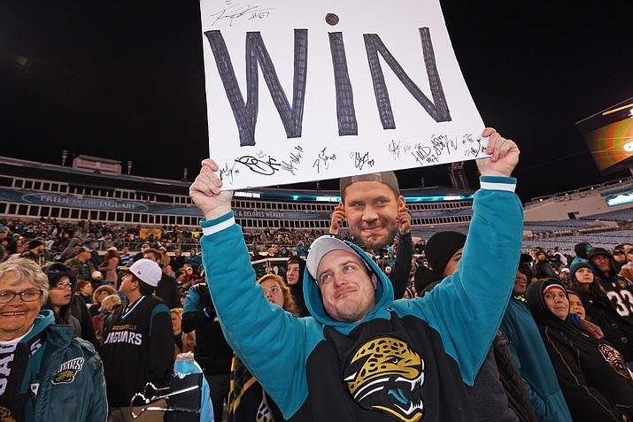 Jaguar fan John Taylor holds his player signed Win sign as he waits in the stands for the Jaguars return to Jacksonville as another fan holds a Blake Bortles big head behind him. Fans gathered at EverBank Field in Jacksonville, Fla. to celebrate a win over the Pittsburgh Steelers Sunday, Jan. 14, 2018. (Bob Self/Florida Times-Union via AP)