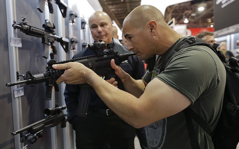 FILE - In this Jan. 14, 2014, file photo, John Montenegro of the Los Angeles Police Department S.W.A.T. team, examines a Sig Sauer MPX-K short barrel submachine gun during the Shooting Hunting and Outdoor Trade Show in Las Vegas. The largest gun industry trade show will be taking place in Las Vegas Jan. 23-26 just a few miles from where a gunman carried out the deadliest mass shooting in modern U.S. history. (AP Photo/Julie Jacobson, file)