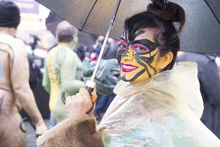 This photo provided by Andy Golub shows a nude model in a see-through poncho poses with her umbrella in the rain and cold during the Polar Bear Paint body-painting event in New York City’s Times Square on Saturday Feb. 10, 2018. (Andy Golub via AP)


