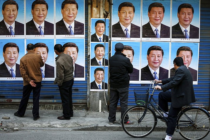 In this March 26, 2016 photo, people look at a building covered in posters of Chinese President Xi Jinping in Shanghai. As China prepares to approve constitutional changes Sunday, March 11, 2018, to allow Xi to rule indefinitely, signs of dissent and satire have been all but snuffed out. (Chinatopix via AP)