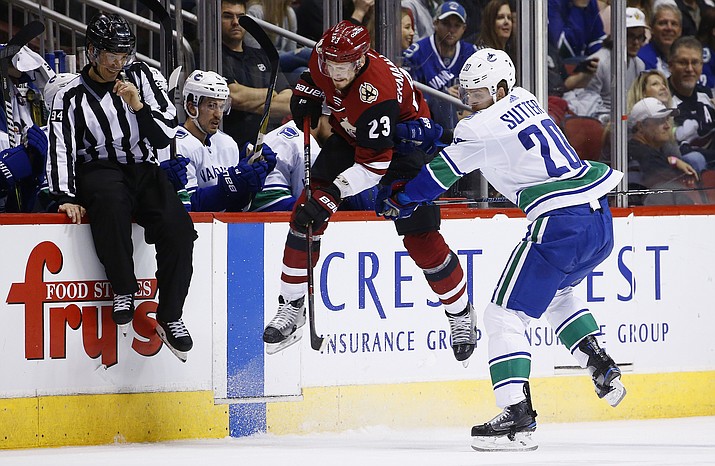Vancouver Canucks center Brandon Sutter (20) checks Arizona Coyotes defenseman Oliver Ekman-Larsson (23) into the boards as linesman Bryan Pancich (94) braces for the hit during the first period of an NHL hockey team Sunday, March 11, 2018, in Glendale. (Ross D. Franklin/AP)