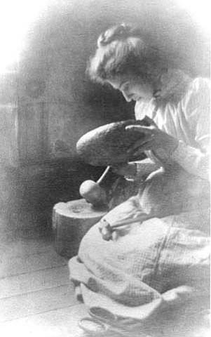 MARY COLTER AT AGE 23 MAKING A METAL BOWL. WEARING CALICO DRESS. SOFT FOCUS. CIRCA 1892.