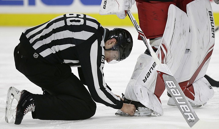 An official removes the puck lodged in Carolina Hurricanes goalie Cam Ward's skate during the first period of the team's NHL hockey game against the Arizona Coyotes in Raleigh, N.C., Thursday, March 22, 2018. Ward inadvertently crossed the goal line while the puck was stuck in his skate which was ruled a goal for the Coyotes. (AP Photo/Gerry Broome)