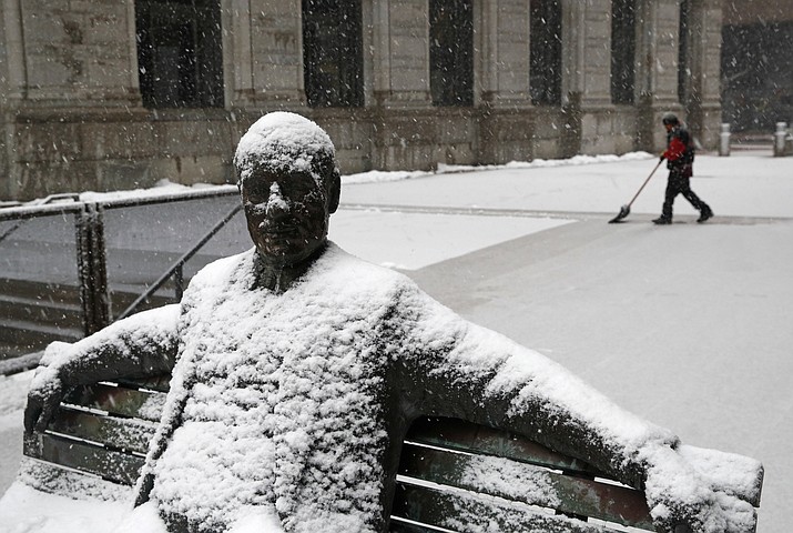Snow sticks to a statue of a man sitting on a park bench as a worker shovels a light snowfall Wednesday, March 21, 2018, in Baltimore. A spring nor'easter targeted the Northeast on Wednesday with strong winds and a foot or more of snow expected in some parts of the region. (AP Photo/Patrick Semansky)

