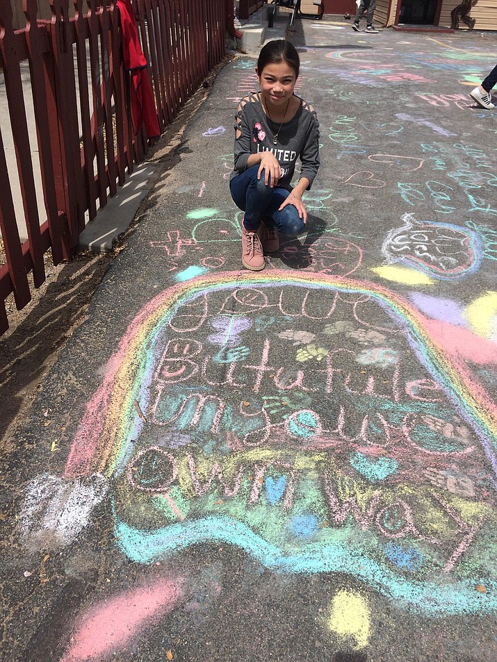 Misora Acor, a fourth-grader, stoops in front of her “Chalk for Change” creation. (Nanci Hutson/Courier)