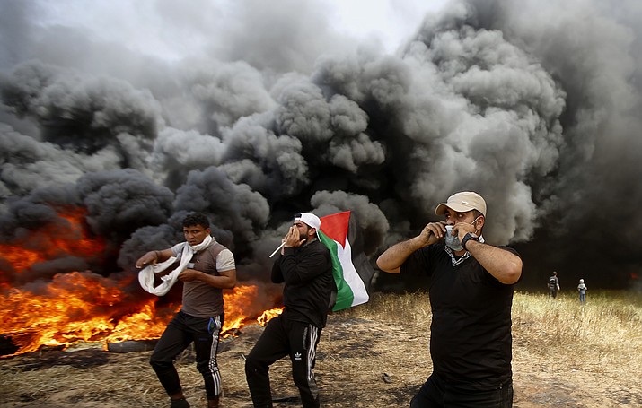 Palestinian protesters chant slogans next to burning tires during clashes with Israeli troops along Gaza's border with Israel, east of Khan Younis, Gaza Strip, Friday, April 6, 2018. Palestinians torched piles of tires near Gaza's border with Israel on Friday, sending huge plumes of black smoke into the air and drawing Israeli fire that killed one man in the second large protest in the volatile area in a week. (AP Photo/Adel Hana)

