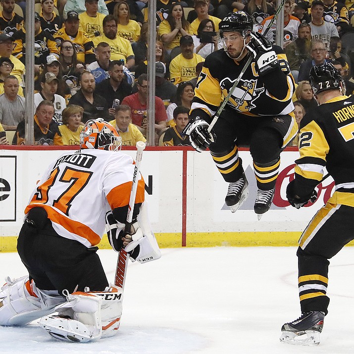 Pittsburgh Penguins' Sidney Crosby (87) leaps out of the way of a shot from the point against Philadelphia Flyers goaltender Brian Elliott, left, during the second period in Game 2 of an NHL first-round hockey playoff series in Pittsburgh, Friday, April 13, 2018. (AP Photo/Gene J. Puskar)

