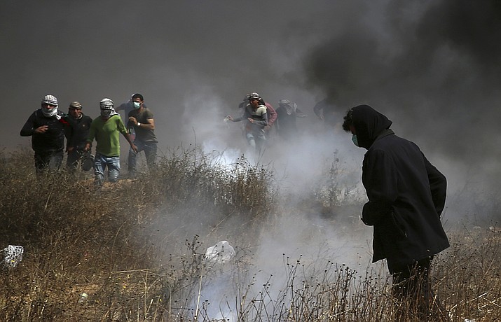 Palestinian protesters run to cover from teargas fired by Israeli troops after they burn tires near the fence during a protest at the Gaza Strip's border with Israel, east of Khan Younis, Friday, April 27, 2018. Palestinians converged on the Gaza border with Israel for a fifth round of weekly protests Friday, some throwing stones and burning tires, as a top U.N. official urged Israel to refrain from using excessive force against them. (AP Photo/Adel Hana)

