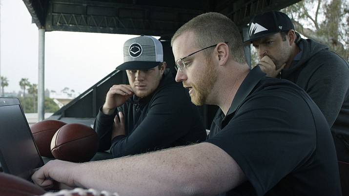 In this April 19, 2018, photo provided by Wilson Sporting Goods, quarterback Sam Darnold, left, and his mentor, former quarterback Jordan Palmer, right, look on as Wilson Labs engineer Dan Hare explains data gathered from throwing a football using the Wilson Connected Football System, at San Clemente High School in San Clemente, Calif. Darnold, the New York Jets rookie quarterback, was at his old stomping grounds in California last month tossing “smart” footballs equipped with computer chips with Palmer, that were calculating his every throw. (Wilson Sporting Goods via AP)