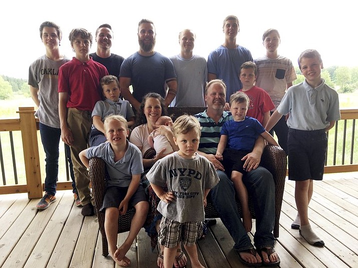 In a photo from May 30, 2018, the Schwandt family poses for a photo at their farm in Lakeview, Mich. Standing from left are Tommy, Calvin, Drew, Tyler, Zach, Brandon, Gabe, Vinny and Wesley. Seated, starting at upper left are Charlie, Luke, mother Kateri holding Finley, father Jay with Tucker and Francisco in the foreground. The 14-boy family ranges in age from 2 months to 25 years. And no girls. (AP Photo/Mike Householder)

