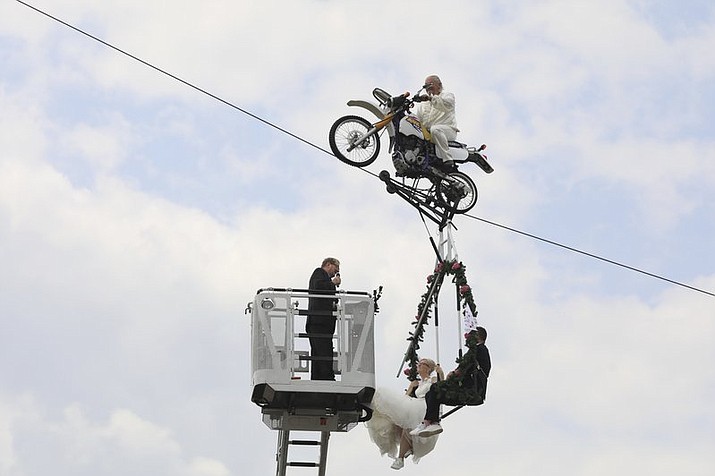 Pastor Stefan Gierung, left, stands in a cage atop of a fire service ladder in front of bride Nicole Backhaus, center, and groom Jens Knorr, right, both sitting in a swing dangling under a motorcycle with artist Falko Traber, top, during the wedding ceremony atop a tightrope in Stassfurt, Germany, Saturday, June 16, 2018. (Peter Gercke/dpa via AP)

