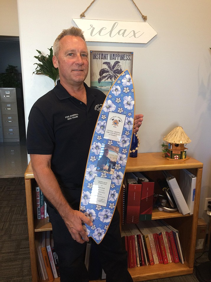 Central Arizona Fire and Medical Authority Fire Marshal Rick Chase with his surf board award honoring him for 18 years with the Fire Pal program. The certificate was presented to him at an authority board meeting on Monday, June 25. (Nanci Hutson/Courier)