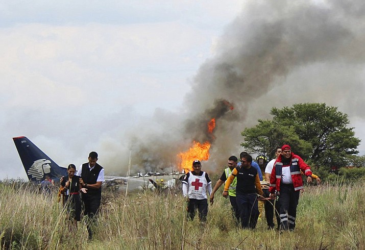 Red Cross workers and rescue workers carry an injured person on a stretcher, right, as airline workers, left, walk away from the site where an Aeromexico airliner crashed in a field near the airport in Durango, Mexico, Tuesday, July 31, 2018. The jetliner crashed while taking off during a severe storm, smacking down in a field nearly intact then catching fire, and officials said it appeared everyone on board escaped the flames. (Red Cross Durango via AP)
