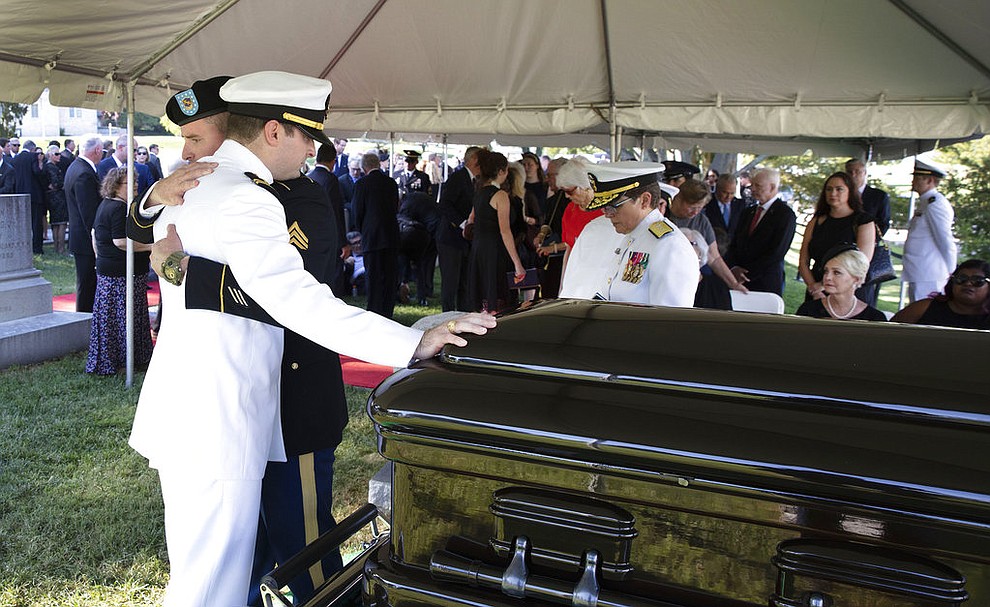 In this image provided by the family of John McCain, Jimmy McCain hugs his brother Jack McCain, touching casket, as Cindy McCain, watches during a burial service for Sen. John McCain, R-Ariz., at the cemetery at the United States Naval Academy in Annapolis, Md., Sunday, Sept. 2, 2018  (David Hume Kennerly/McCain Family via AP)