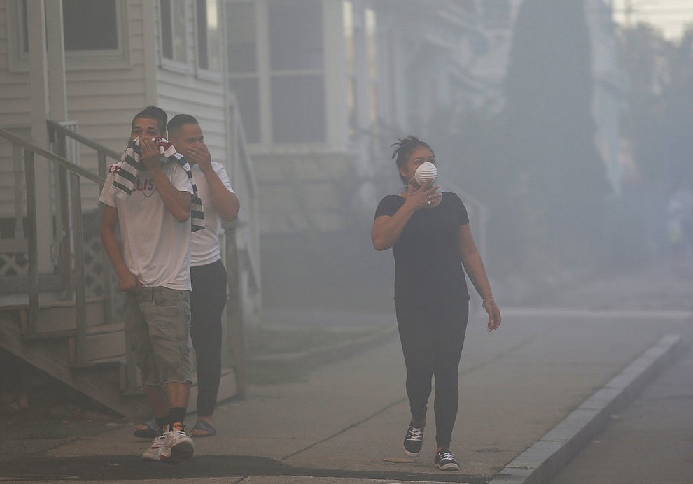 People cover their faces to protect themselves from heavy smoke from a fire on Bowdoin Street in Lawrence, Mass., Thursday, Sept. 13, 2018. The company that owns Columbia Gas says its crews are performing safety checks after a series of fires and explosions erupted in three communities north of Boston. (Jessica Rinaldi/The Boston Globe via AP)