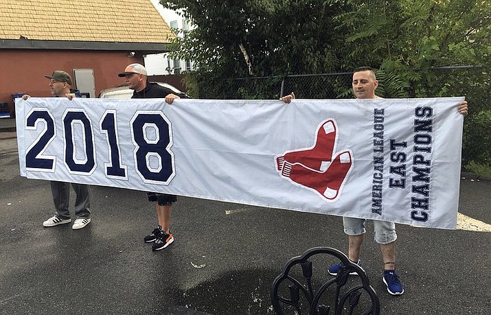 In this Tuesday, Sept. 18, 2018 photo, friends hold a banner they found in Somerville, Mass., that proclaims the Boston Red Sox are the 2018 American League East Champions, though the team has not yet clinch the division. A Red Sox spokesman said the banner apparently fell off a vendor’s delivery truck, and planned to send a courier to retrieve the banner Wednesday. (Ted Daniel/Boston 25 News via AP)

