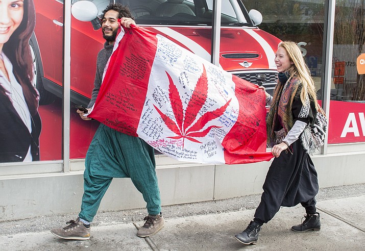 People hold up a Canadian flag with a marijuana logo on it outside a government cannabis store in Montreal, Wednesday, Oct. 17, 2018. Canada became the largest country with a legal national marijuana marketplace as sales began early Wednesday. (Graham Hughes/The Canadian Press via AP)